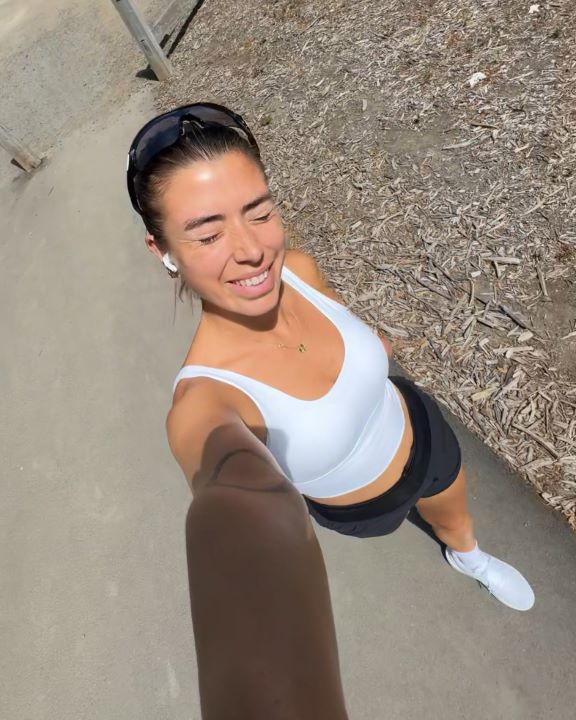 Selfie of Eliza Boyd running on the street squinting into the sun wearing a white singlet and black shorts